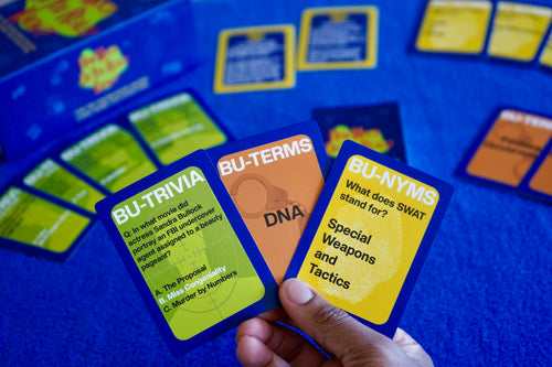 Hand holding educational card games with questions on a blue background
